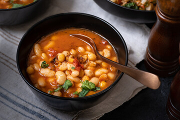 Vegan bean and garbanzo soup served in black bowl on dark backround