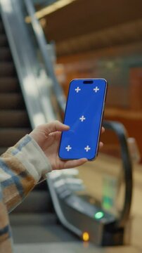 Vertical Screen: Woman showing a smartphone with chroma key blue screen and tracking markers while standing still on an escalator in a subway station