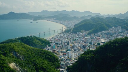 Panoramic view of a coastal city with a long bridge and mountains in the background