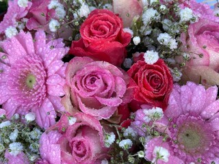 Blumen in Rosa und Rot mit Rosen und Gerbera nach Beerdigung auf dem Friedhof mit Regentropfen und Schleierkraut