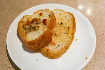 close up of two small pieces of garlic bread toast with butter on a white plate. There is copy space. 