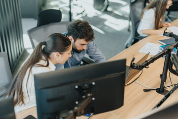 Two business people engaged in a collaborative work session at a contemporary office. They are focused on a computer screen, representing teamwork, efficiency, and productivity in a corporate setting.