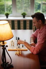 A person in a pink shirt smiles while making a move on a chessboard. The scene is set in cozy...