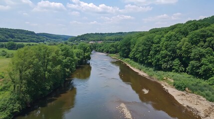 Fototapeta premium A serene river flows through a lush green landscape under a bright blue sky