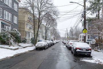 Snow-covered residential street with parked cars and houses in Brighton, Massachusetts, USA
