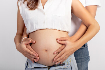 Happy family Asian couple on white background, husband is embracing his wife from back, they gently touching hands on belly while stand together. Pregnant woman mother with big tummy.