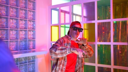 Caucasian dancer dancing while diverse friend looking at footstep in neon light at night club. Back view of multiethnic hipster moving to freestyle music with happy man looking at camera. Regalement.