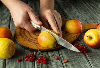 Hands expertly cut ripe apples on a rustic wooden board surrounded by vibrant citrus fruits. The...