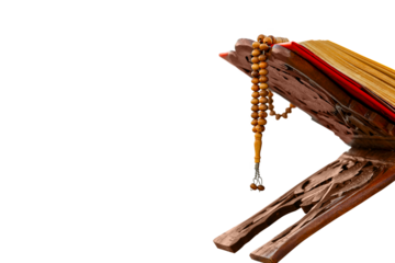 A close-up shot of an open Quran on a traditional wooden stand (rahle) with a string of prayer beads (tesbih) laid on top. The image is set against a plain gray background, highlighting the Quran and 