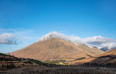 Landscape photography of mountain Beinn Dorain, winter weather, Scotland, Glen Orchy, UK, rocky hill, hiking trail, blue sky with clouds, snow on the mountain peak