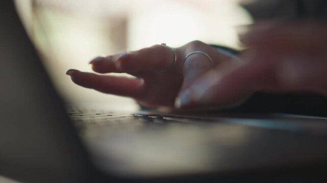 Close-up of elegant fingers with rings typing on laptop keyboard, showcasing polished nails in a relaxed outdoor setting, soft focus on laptop, with blurred background