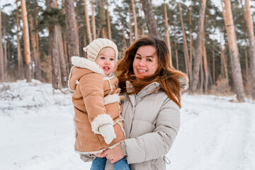 Fototapeta premium A mother with her little child daughter in a snowy winter forest.