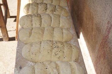Handmade and homemade sourdough bread loaves sprinkled with white and black sesame seeds carved into slices in a row outdoors ready to be baked