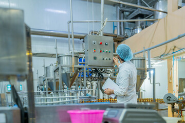 A professional factory worker inspects and monitors canned food processing on an automated assembly line in a modern industrial plant for quality assurance.