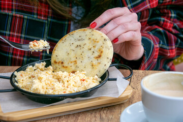 a close up image of a women eating Colombian scrambled eggs with arepa in mediterranean restaurant 