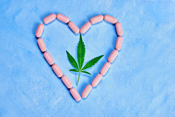 a cannabis leaf lies inside a heart of pink pills on a blue background, close-up, concept of medical use, what do you choose - pills or a natural product?