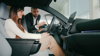 Beautiful Caucasian female sitting inside of new vehicle at drivers seat. Woman carefully listening...