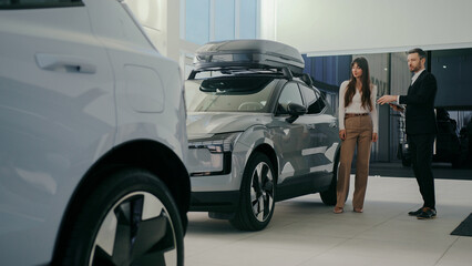 Cute Caucasian couple standing next to modern car and listening to manager talking. Bearded male...