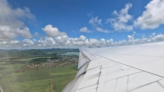 Large airplane climbing after takeoff from Mauritius airport. View from the window above the wing, showing the island, ocean, and low clouds.