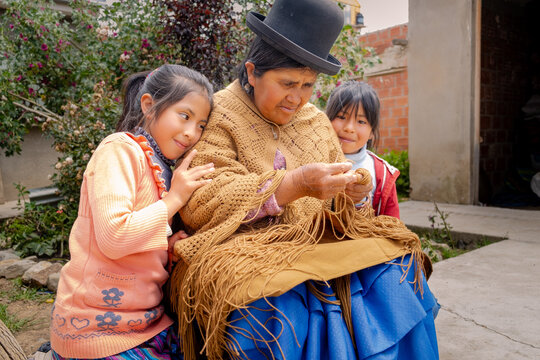 adult aymara woman in pollera working on handcrafted wool textiles with her granddaughters at home - work concept