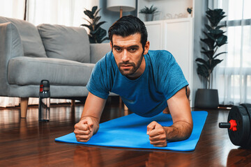 Fototapeta premium Athletic and sporty man doing plank on fitness mat during home body workout exercise session for fit physique and healthy sport lifestyle at home. Gaiety home exercise workout training.