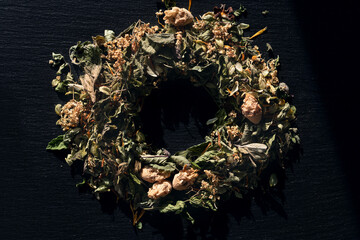 A wreath of dried herbal tea in front of a dark slate plate. Individual ingredients of the herbal...