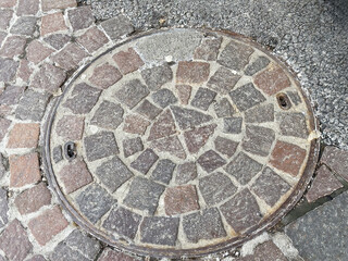 Round cobblestone manhole cover on textured pavement