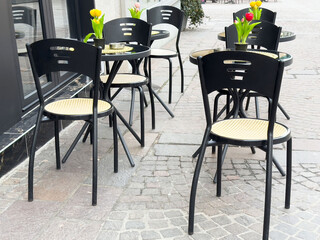 Outdoor café seating with black chairs and tulip-adorned tables on a cobblestone street