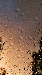 A photograph of raindrops on a glass window with a soft ochre and blue background. The blurred, moody atmosphere creates a tranquil and dreamy feel, perfect for weather and abstract-themed designs