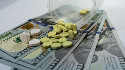 Scattered pills on hundred-dollar bills placed on a white table. Medical treatment concept. Opioid...