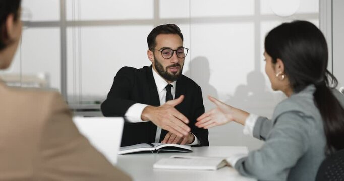 Hispanic businessman, boss or leader shaking hands with colleague or stakeholder seated at conference table. Business parties expressing mutual agreement, closing successful negotiation with handshake