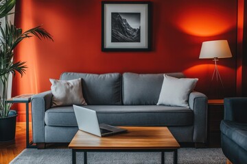 Modern living room with gray sofa, laptop, and red wall.
