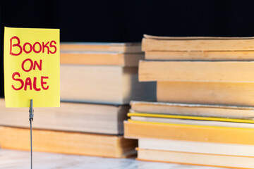 Books on sale advertisement on a metal stand with a background of stacked books