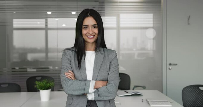 Young 30s Arabian businesswoman dressed in formal jacket posing for camera stand in modern conference room. Successful, self-assured company employee. Human resource, headhunter or CEO office portrait