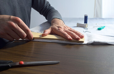 Manos de hombre haciendo marca sobre tela con regla recta para corte y costura a mano. 