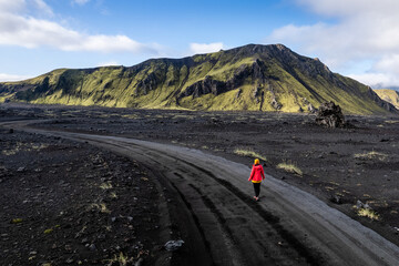 Stunning aerial image showcasing a woman standing over volcanic crater surrounded Landmannalaugar mountains and by hills and wilderness, emphasizing raw beauty and unique geology of volcanic regions