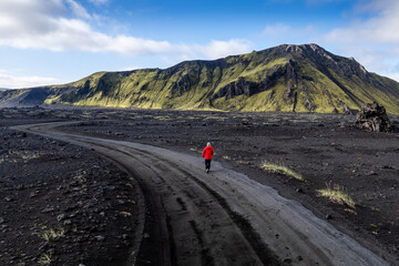 Stunning aerial image showcasing a man standing over volcanic crater surrounded Landmannalaugar mountains and by hills and wilderness, emphasizing raw beauty and unique geology of volcanic regions