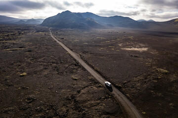 Aerial perspective of a car navigating a sparse basalt road Landmannalaugar in Iceland, surrounded by barren landscapes and bathed in warm sunlight