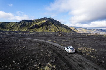Aerial perspective of a car navigating a sparse basalt road Landmannalaugar in Iceland, surrounded by barren landscapes and bathed in warm sunlight