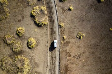 A drone shot showing a white vehicle traveling along a narrow dirt road a desert landscape near Landmannalaugar called Rainbow Mountains in Iceland. Emphasizing isolation, travel, and exploration