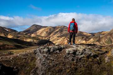 Fototapeta premium Alone hiker stands in a vibrant mountain setting Landmannalaugar, surrounded by colorful hills and dramatic scenery. The scene invokes a sense of adventure, solitude, and connection with wilderness