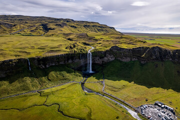 A magnificent aerial view Seljalandsfoss waterfall in Iceland plunges over the edge of green cliffs, surrounded by stunning countryside. The serene landscape captures beauty of untouched nature