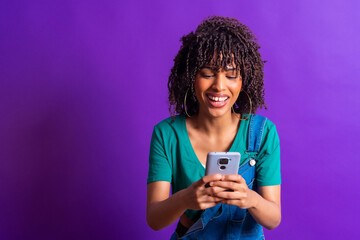 Cheerful young woman using smartphone on purple background