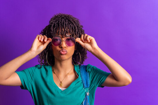 Young woman adjusting sunglasses and pouting on purple background