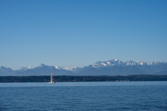 Cool blue winter landscape looking across Puget Sound with the Olympic Mountains in the background, sunny winter day with catamaran sailing on the Salish Sea
