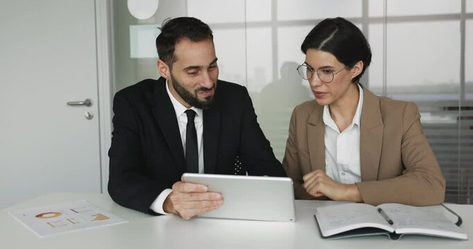 Two professionals lively discussing project details or updates seated at table, identifying trends, review new business tool or software using digital tablet device. Mentor explain tasks to colleague