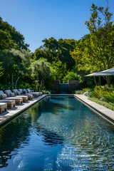 Obraz premium Luxurious Backyard Pool with Lounge Chairs and Waterfall Surrounded by Lush Greenery