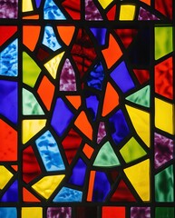 Vibrant stained glass mosaic with multicolored geometric pieces arranged in an abstract pattern, featuring deep reds, blues, greens, and yellows illuminated by light reflections

