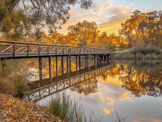 Golden sunset reflects on calm river, wooden bridge, autumn trees.