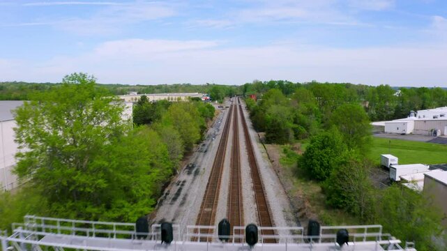Daytime overhead view from a drone of three parallel railroad train tracks near fields and industry in a rural location.
